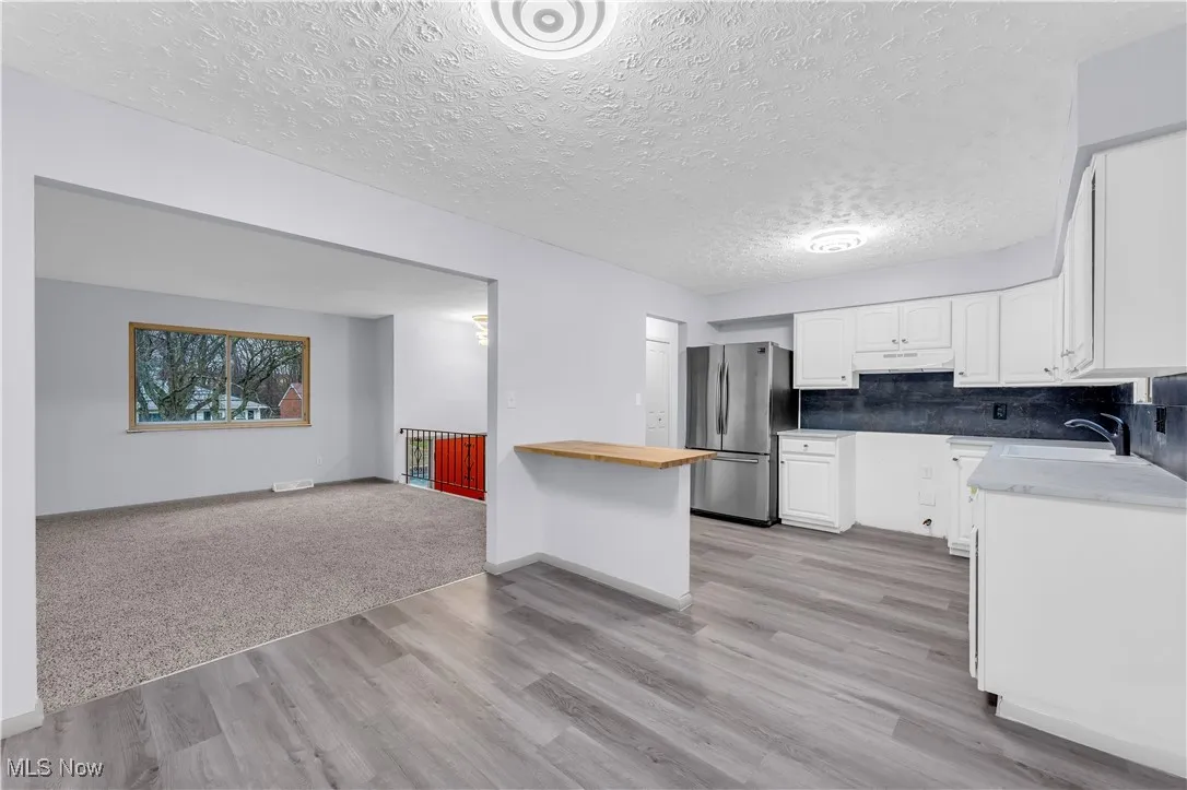 Kitchen featuring open floor plan, white cabinetry, freestanding refrigerator, under cabinet range hood, and a sink