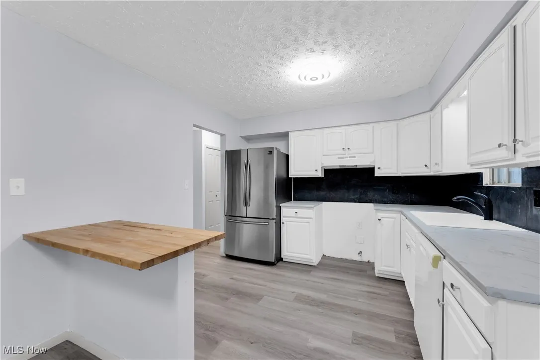 Kitchen with light wood-type flooring, freestanding refrigerator, a textured ceiling, under cabinet range hood, and white cabinetry