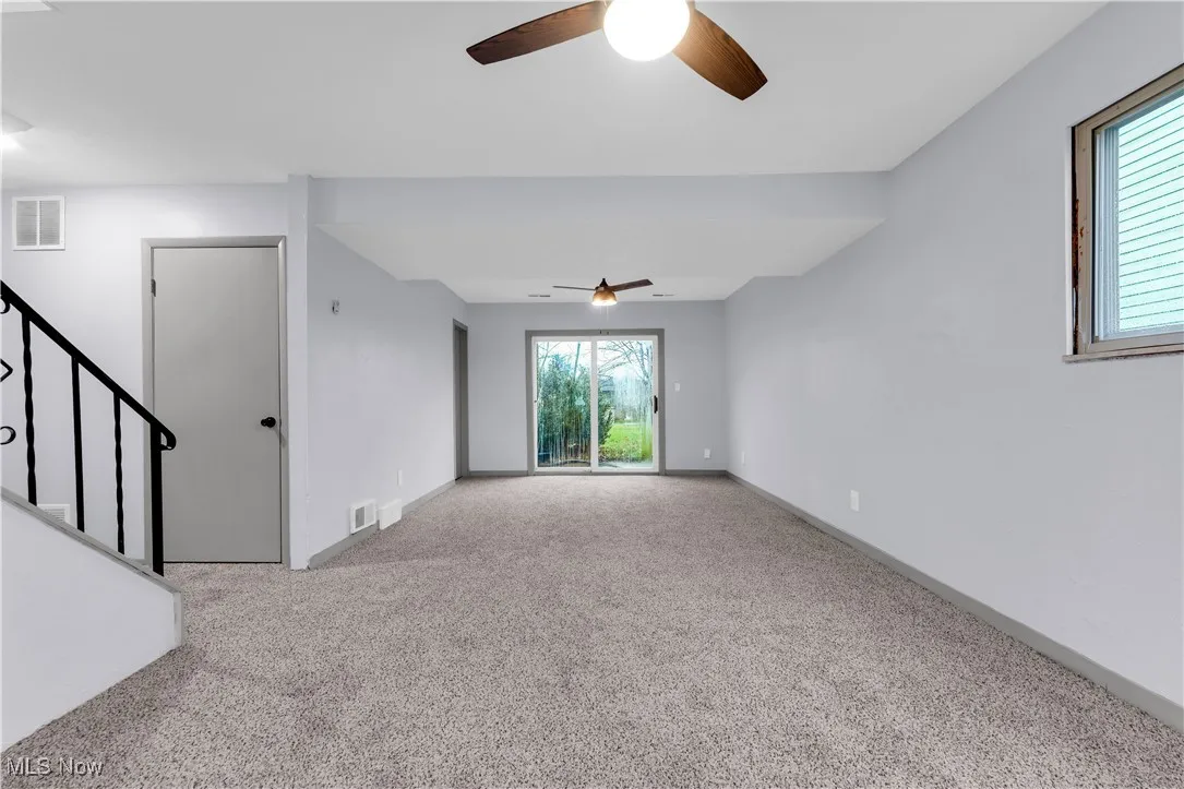Empty room featuring stairway, visible vents, a ceiling fan, and carpet floors
