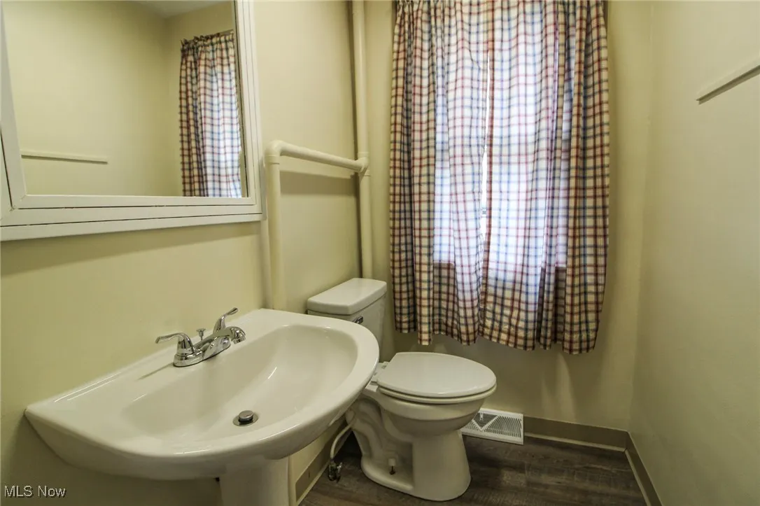 Bathroom with visible vents, baseboards, a sink, toilet, and wood finished floors