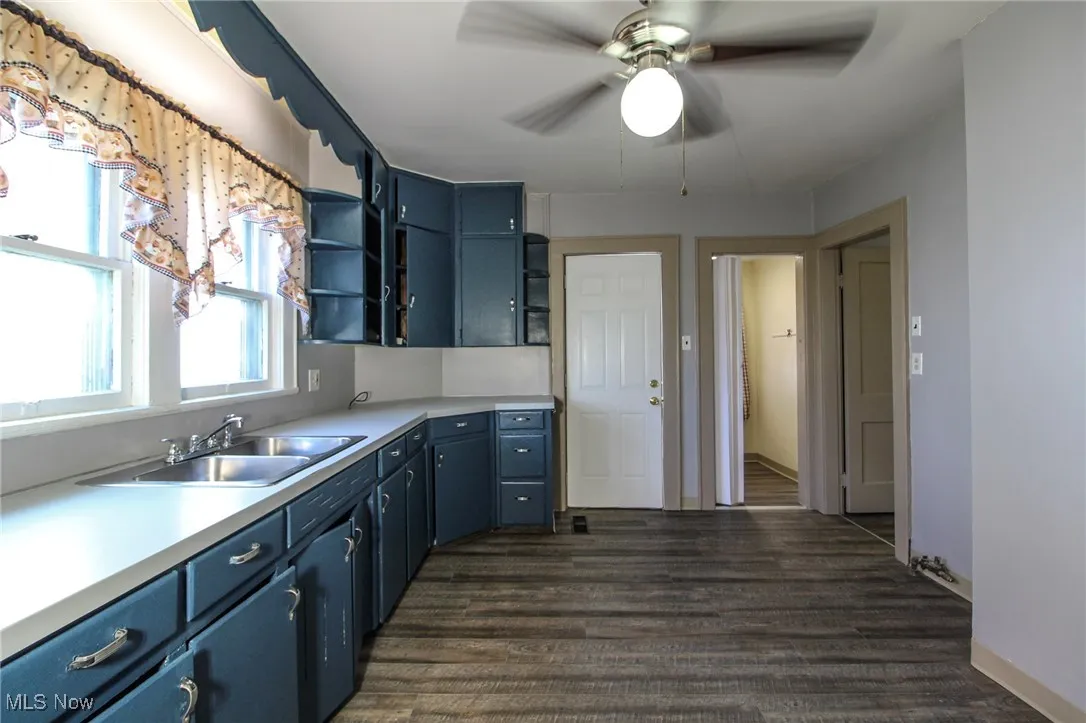 Kitchen featuring open shelves, a sink, a ceiling fan, dark wood finished floors, and blue cabinets
