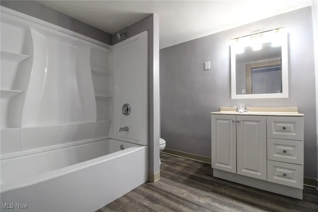 Bathroom with baseboards, shower / washtub combination, toilet, vanity, and wood finished floors