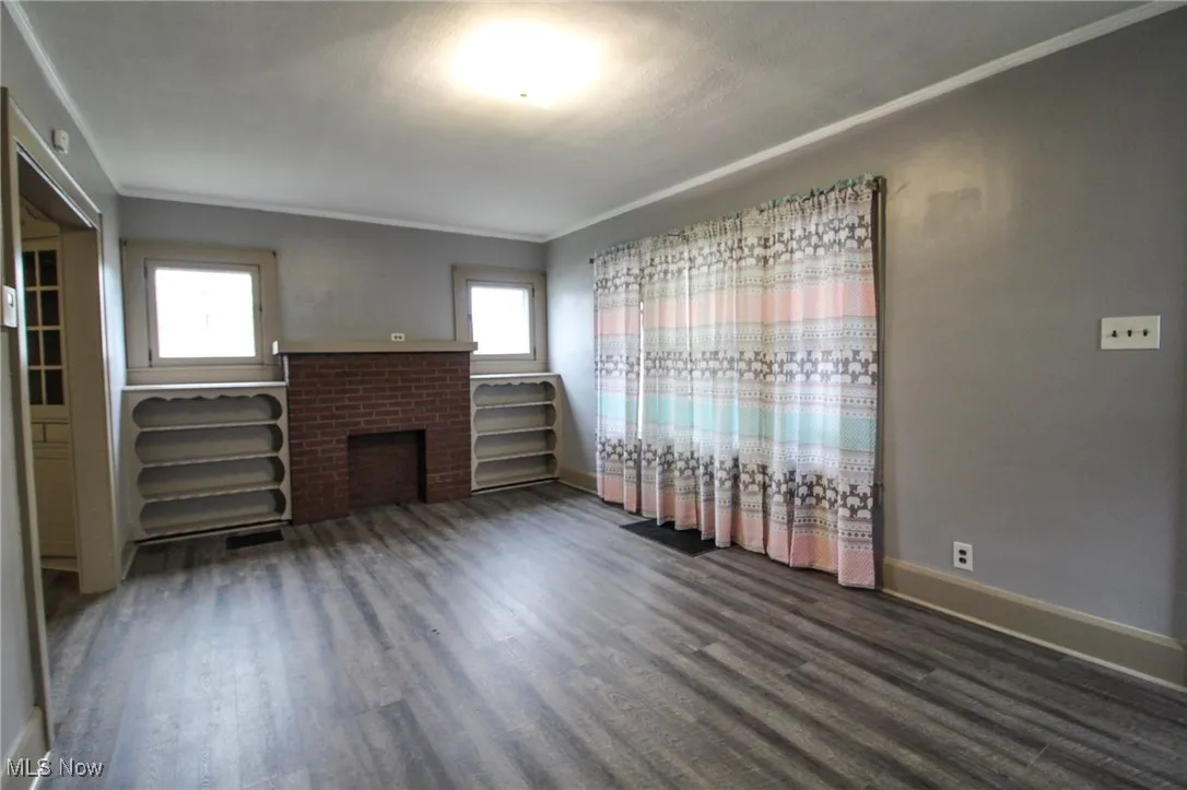 Unfurnished living room with wood finished floors, baseboards, ornamental molding, and a brick fireplace