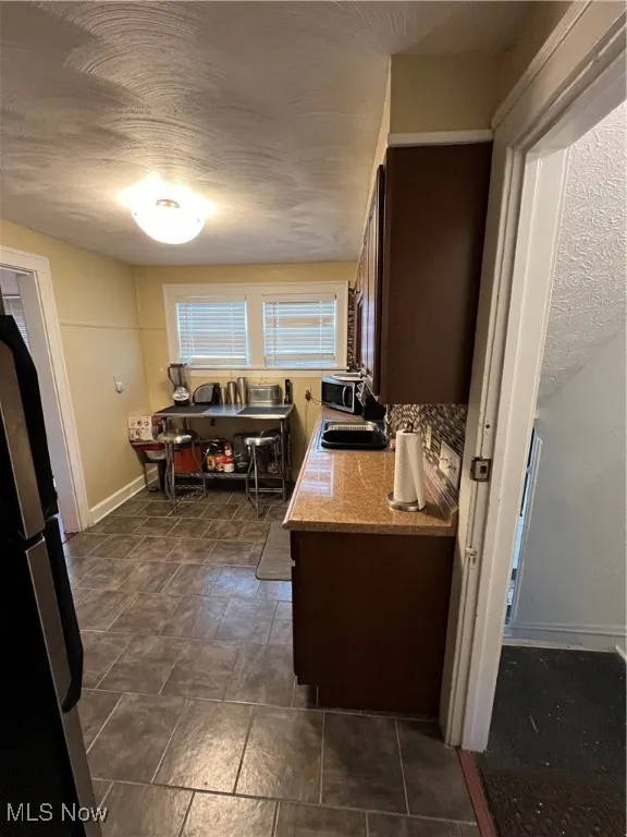 Kitchen with baseboards, refrigerator, light countertops, a textured ceiling, and a sink
