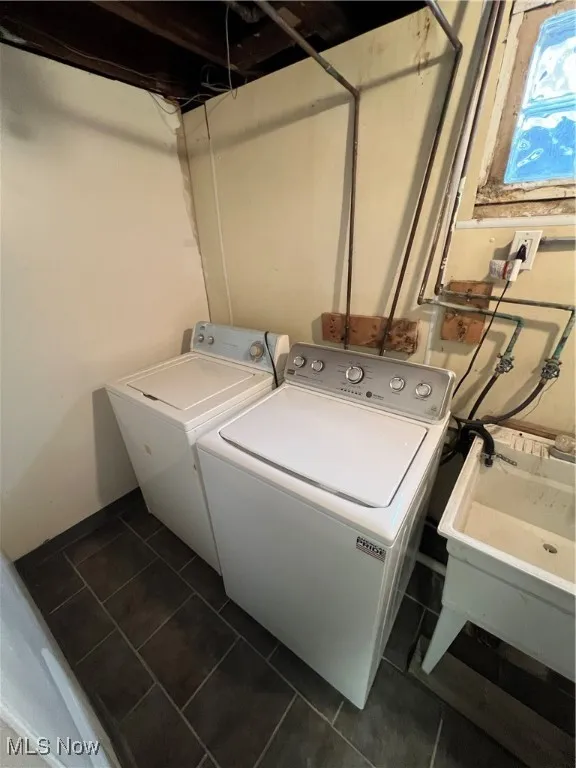 Washroom with dark tile patterned flooring, laundry area, a sink, and washing machine and dryer