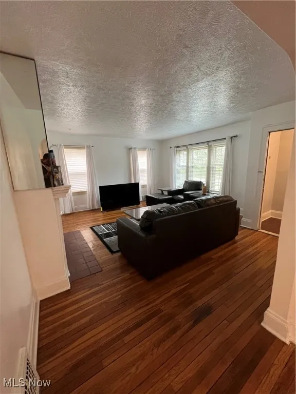 Living room with a textured ceiling, visible vents, hardwood / wood-style floors, and plenty of natural light