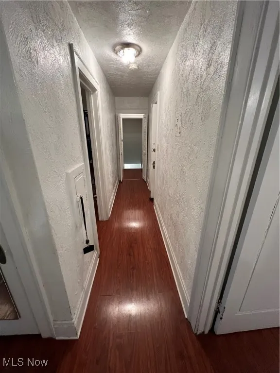 Hall featuring baseboards, wood finished floors, a textured wall, and a textured ceiling