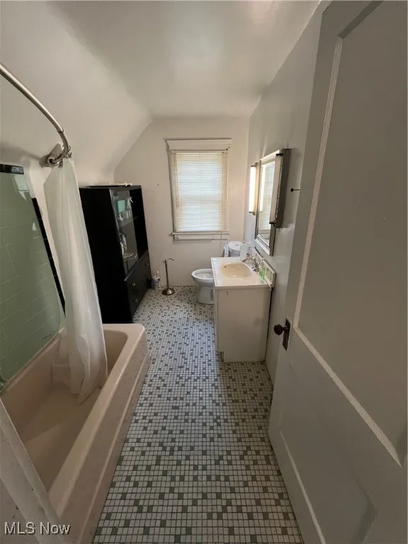 Full bath with vanity, tile patterned floors, shower / bath combination with curtain, toilet, and lofted ceiling