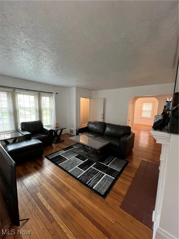 Living area with a textured ceiling, visible vents, hardwood / wood-style flooring, and arched walkways