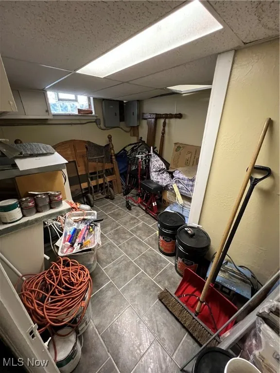 Basement featuring electric panel, tile patterned flooring, and a drop ceiling