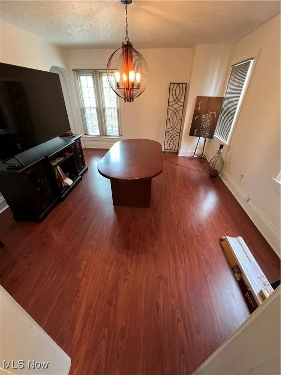 Dining room featuring a textured ceiling, a notable chandelier, dark wood finished floors, and baseboards