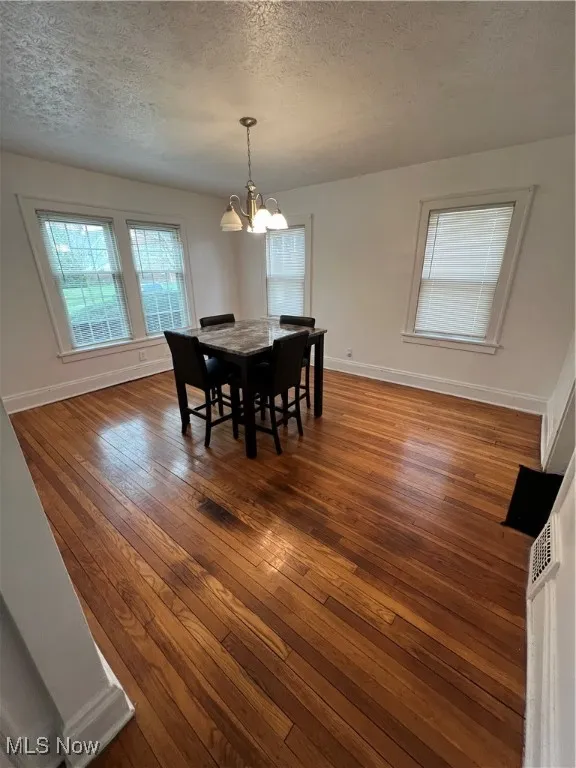 Dining space featuring baseboards, a notable chandelier, dark wood-style flooring, and a textured ceiling