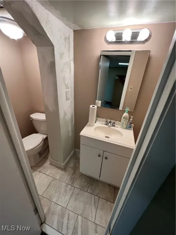 Half bath with toilet, vanity, and marble finish floor