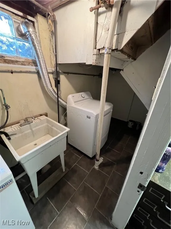 Laundry area with dark tile patterned flooring, laundry area, a sink, and washer / dryer