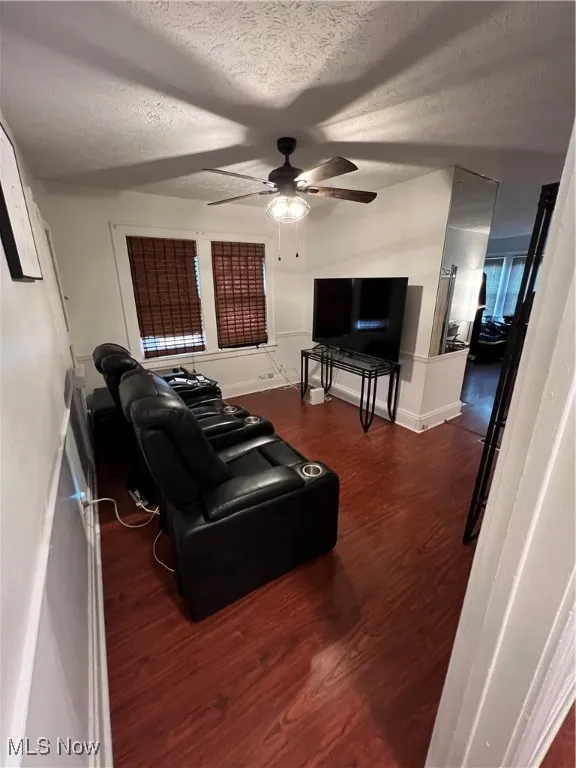 Living area with a textured ceiling, wood finished floors, baseboards, and a ceiling fan