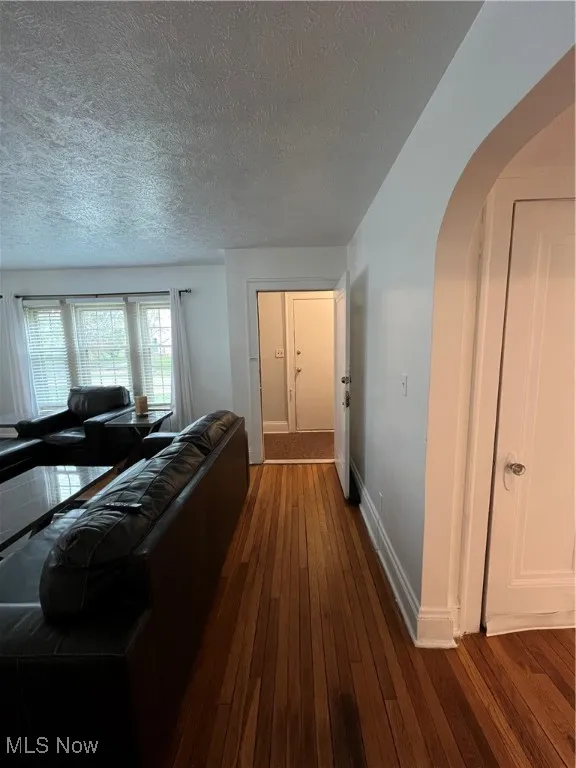 Living room with arched walkways, dark wood-style floors, a textured ceiling, and baseboards