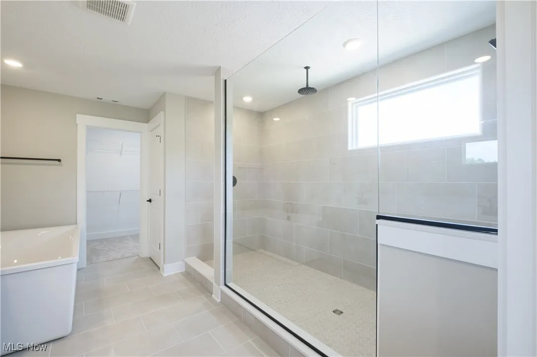 Bathroom with a tile shower, a spacious closet, tile patterned flooring, a textured ceiling, and vanity