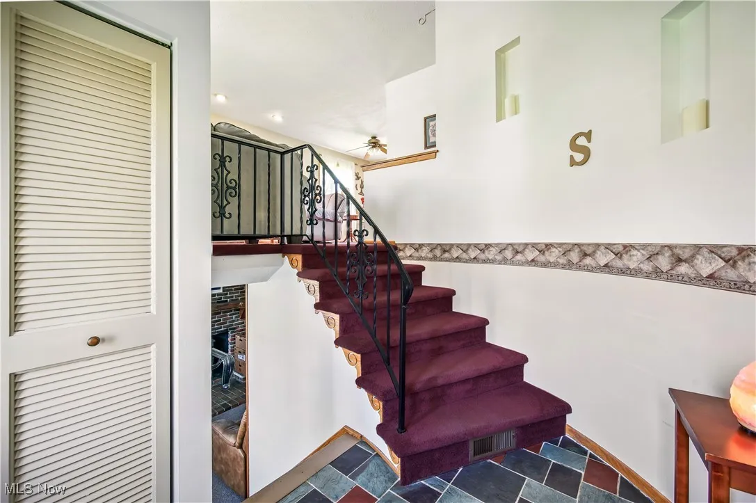 Stairway featuring stone finish flooring, a fireplace, visible vents, and ceiling fan