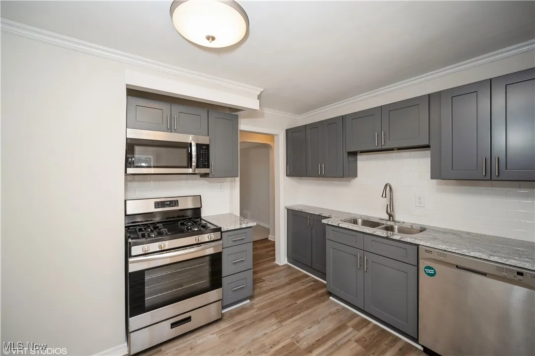 Kitchen with ornamental molding, gray cabinets, a sink, stainless steel appliances, and light wood finished floors