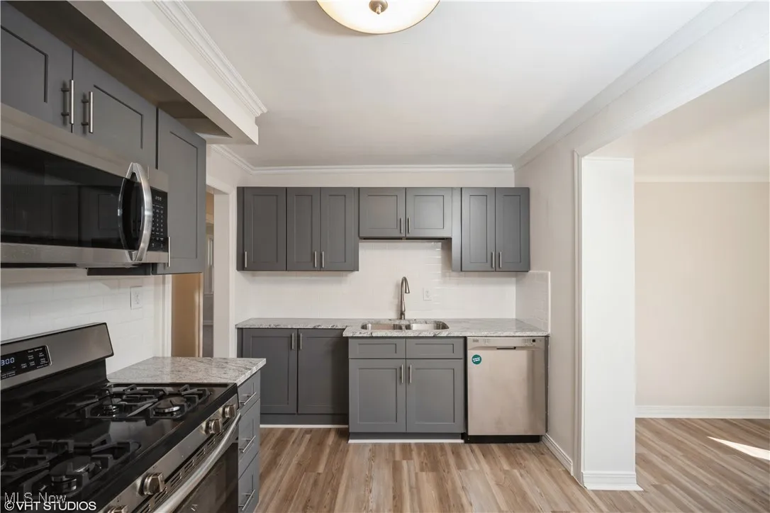 Kitchen with crown molding, light stone countertops, appliances with stainless steel finishes, a sink, and light wood finished floors