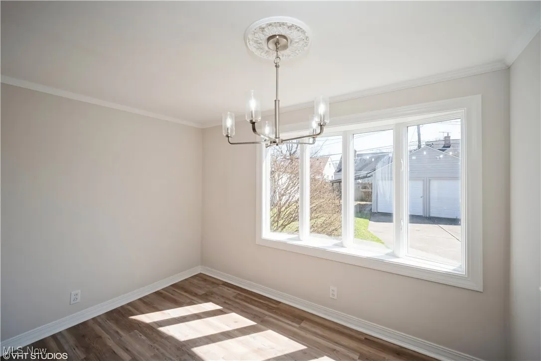 Unfurnished dining area with ornamental molding, baseboards, an inviting chandelier, and wood finished floors