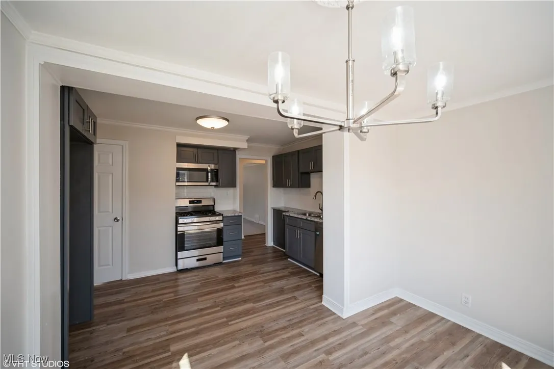 Kitchen with baseboards, ornamental molding, a chandelier, stainless steel appliances, and wood finished floors