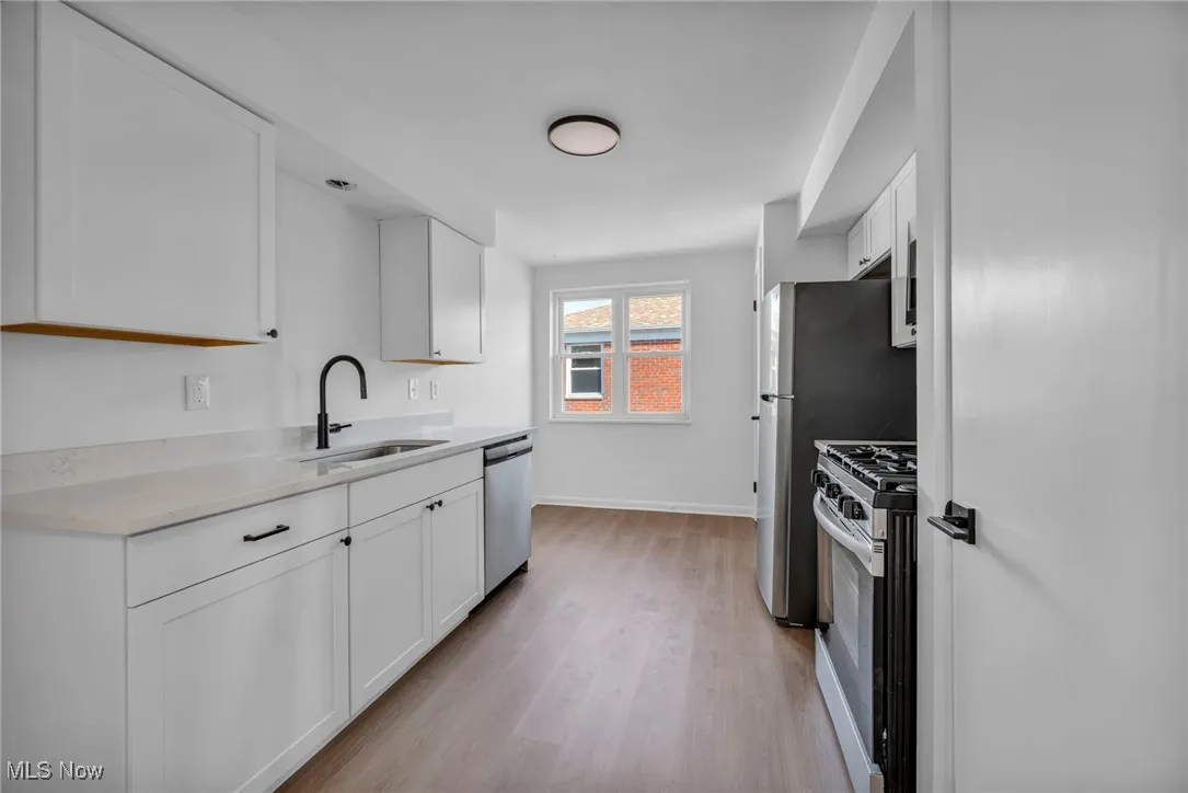 Kitchen featuring range with gas stovetop, light wood-style flooring, white cabinets, stainless steel dishwasher, and a sink