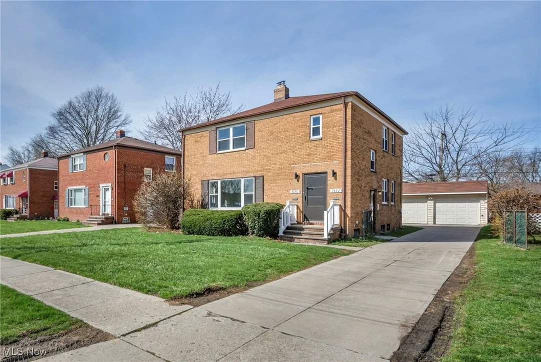 View of front of house with a chimney, a front yard, brick siding, an outbuilding, and a garage