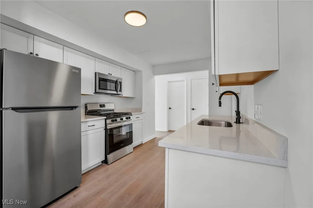 Kitchen with a sink, white cabinets, light wood-type flooring, and stainless steel appliances