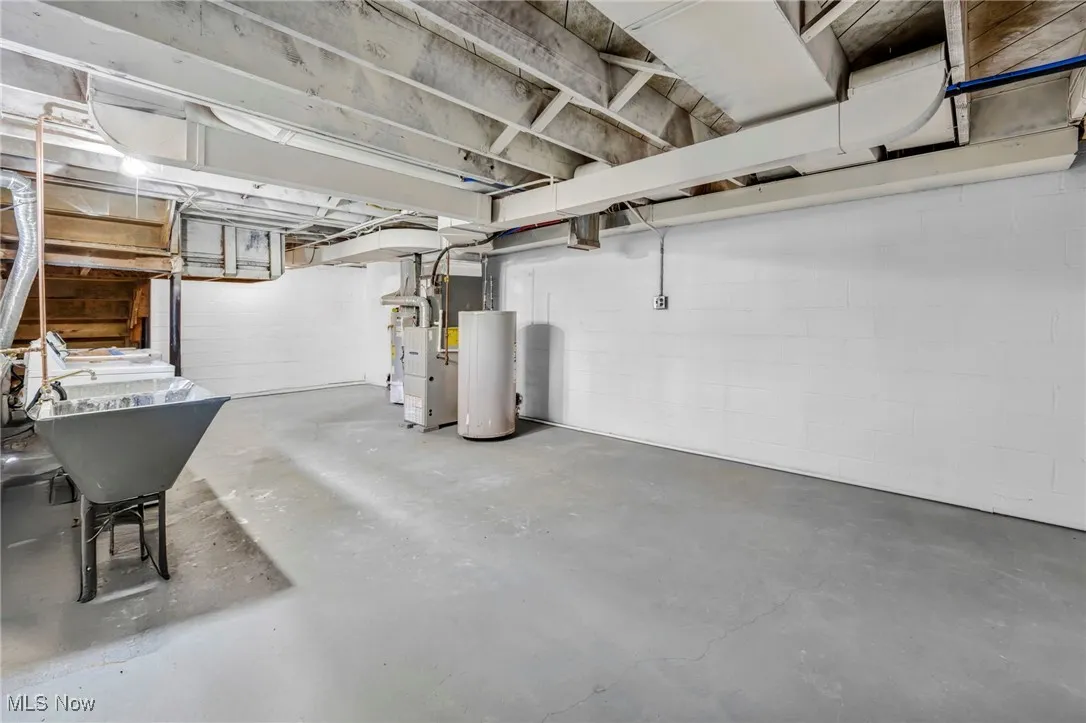 Unfinished below grade area with concrete block wall, gas water heater, and heating unit