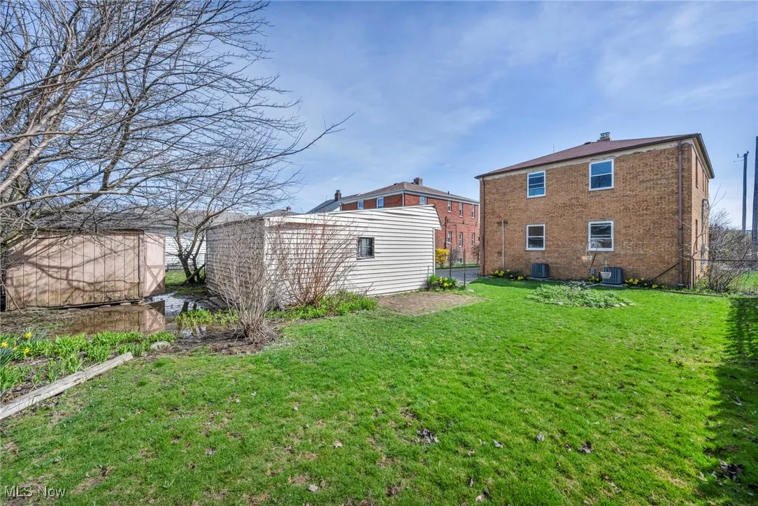 Back of property with a yard, brick siding, an outdoor structure, and central AC unit