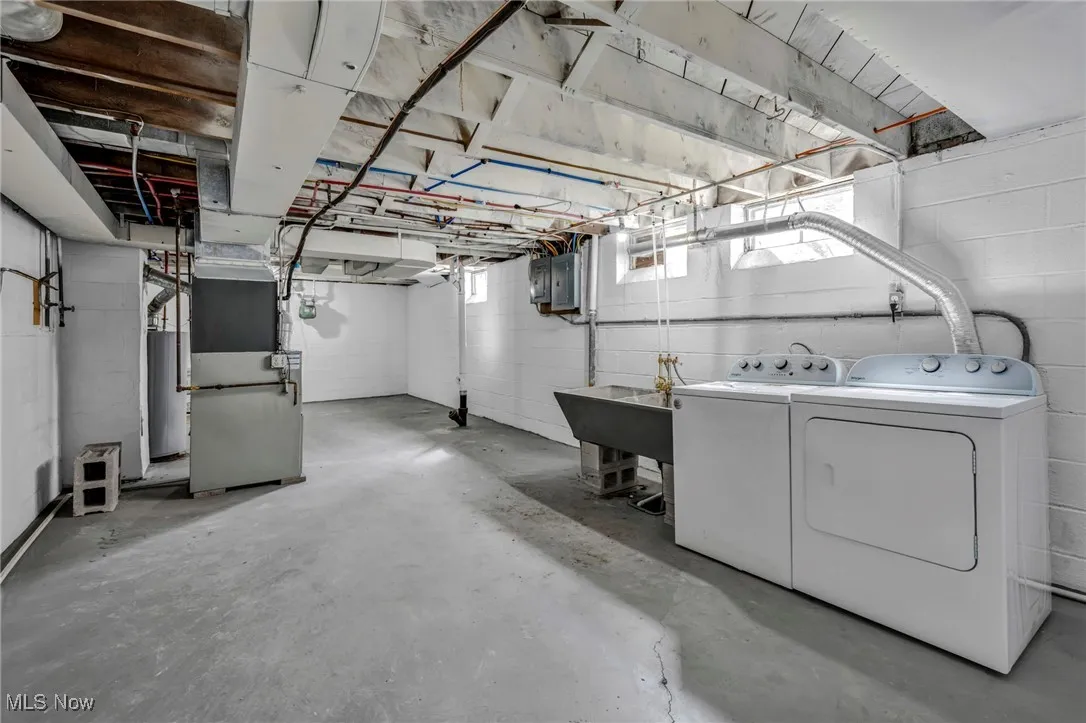 Below grade area with electric panel, a sink, washing machine and dryer, and heating unit