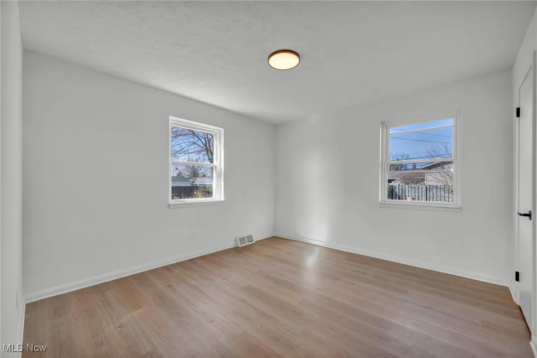 Empty room with a textured ceiling, wood finished floors, baseboards, and visible vents
