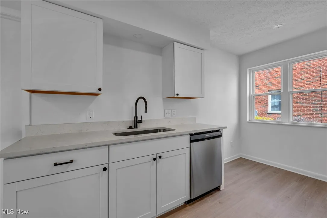 Kitchen with white cabinets, a sink, light wood-type flooring, a textured ceiling, and stainless steel dishwasher