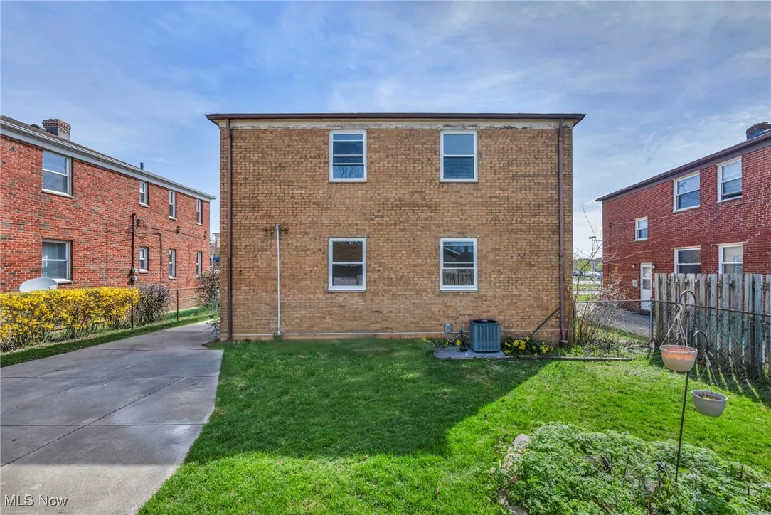 Back of property with central AC, a yard, and brick siding