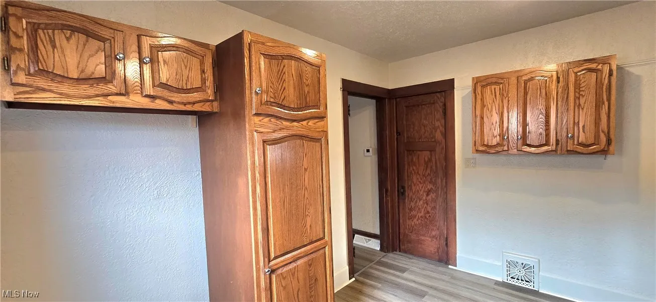 Kitchen with brown cabinetry, light wood-type flooring, visible vents, and a textured ceiling