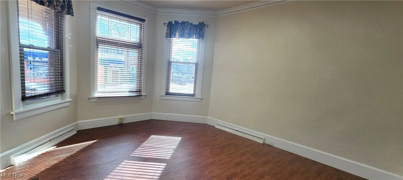 Empty room featuring a baseboard heating unit, crown molding, and dark wood-type flooring