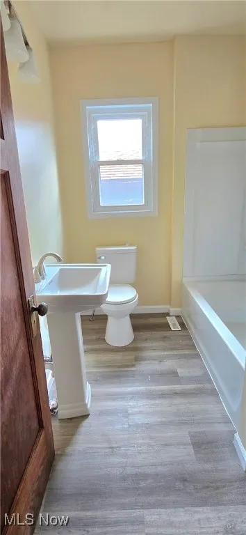 Bathroom featuring baseboards, a bathing tub, toilet, a sink, and wood finished floors