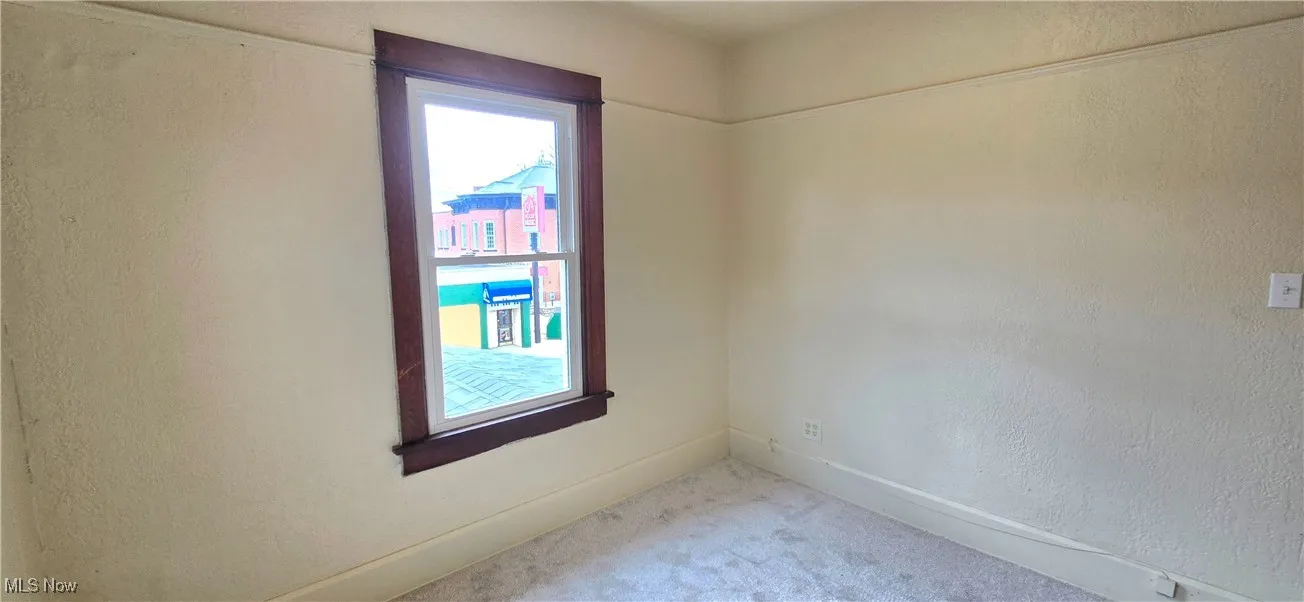 Spare room with light carpet, a textured wall, and baseboards