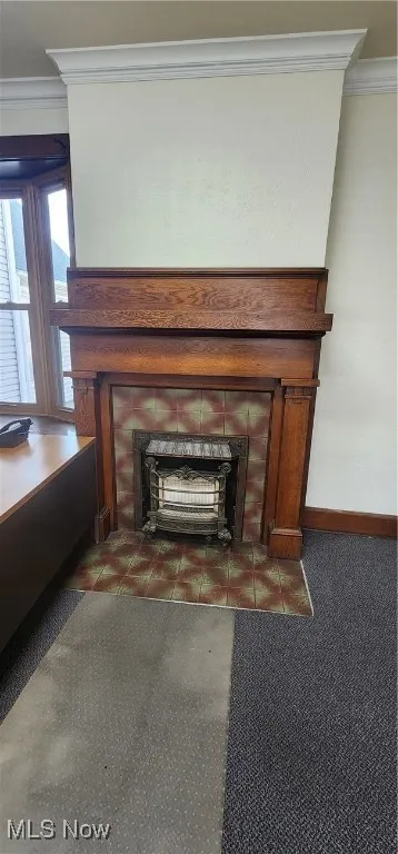 Room details featuring a fireplace, ornamental molding, and dark carpet