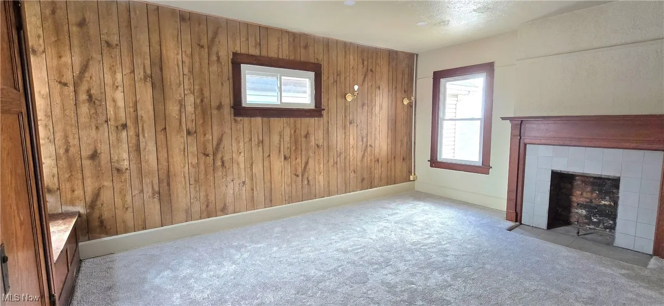 Unfurnished living room featuring baseboards, wood walls, a fireplace, and carpet