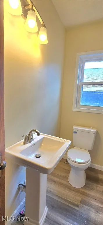 Half bathroom with toilet, wood finished floors, and baseboards