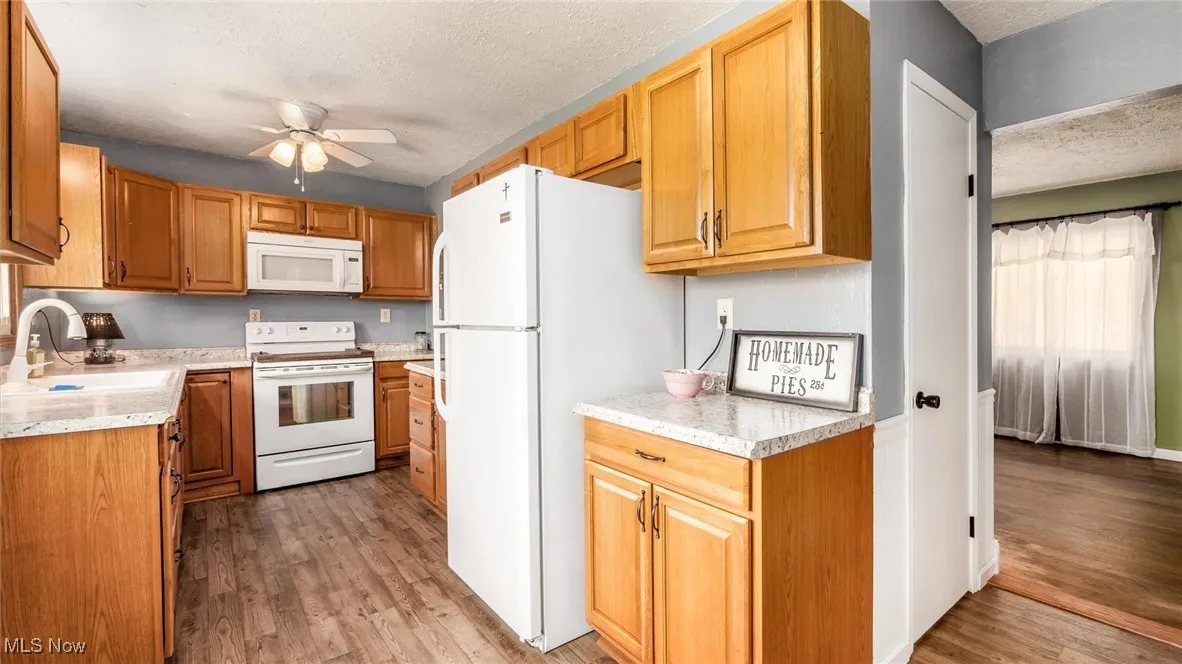 Kitchen with a ceiling fan, light countertops, a sink, and white appliances