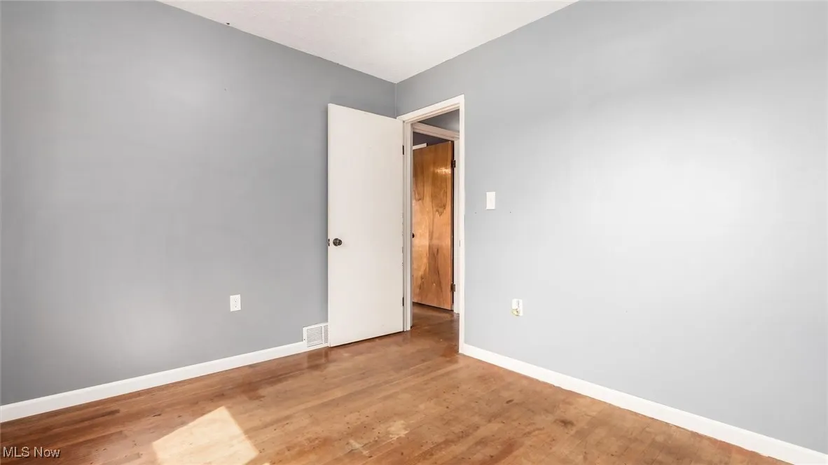 Unfurnished room featuring visible vents, baseboards, and wood finished floors