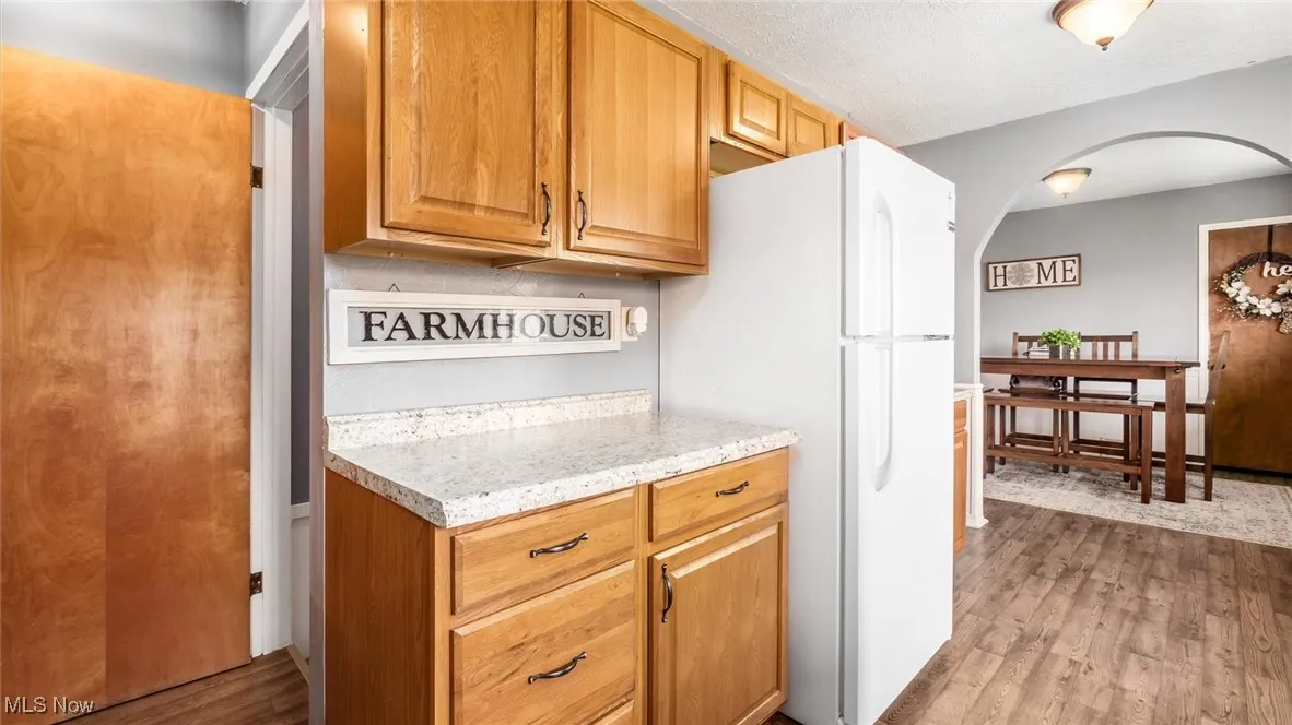 Kitchen with light stone counters, freestanding refrigerator, arched walkways, and wood finished floors