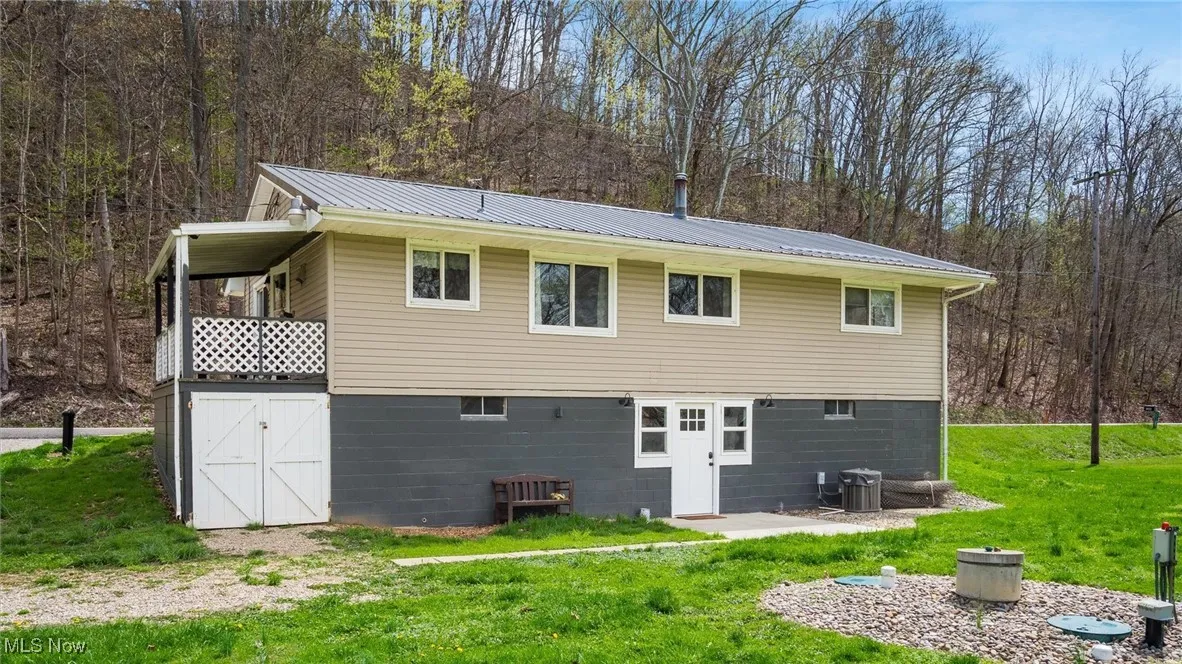 Rear view of property with a yard, metal roof, a forest view, and cooling unit
