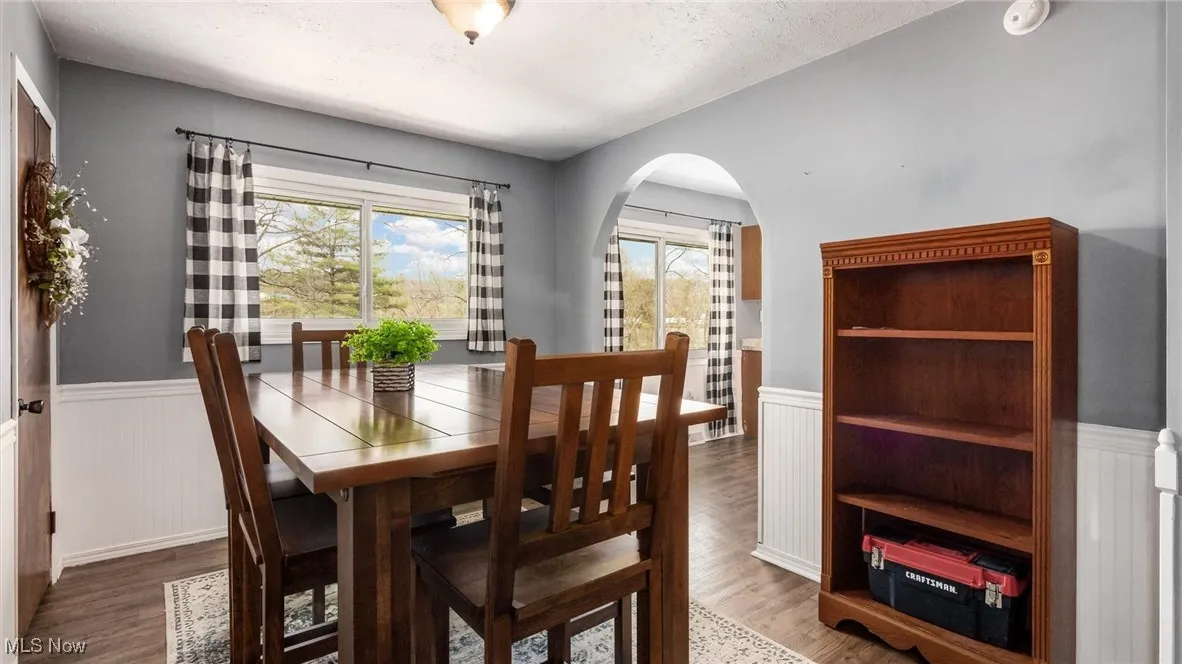 Dining room with arched walkways, wainscoting, a textured ceiling, and wood finished floors