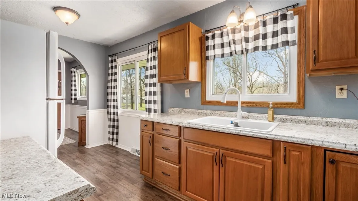 Kitchen featuring brown cabinetry, arched walkways, dark wood-style flooring, and a sink