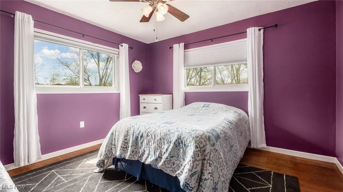Bedroom featuring baseboards, multiple windows, ceiling fan, and wood finished floors