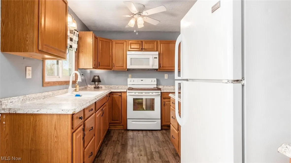 Kitchen with a sink, dark wood-style flooring, light countertops, a ceiling fan, and white appliances